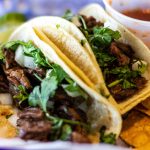 Two carne asada tacos with cilatro and onion on corn tortillas.